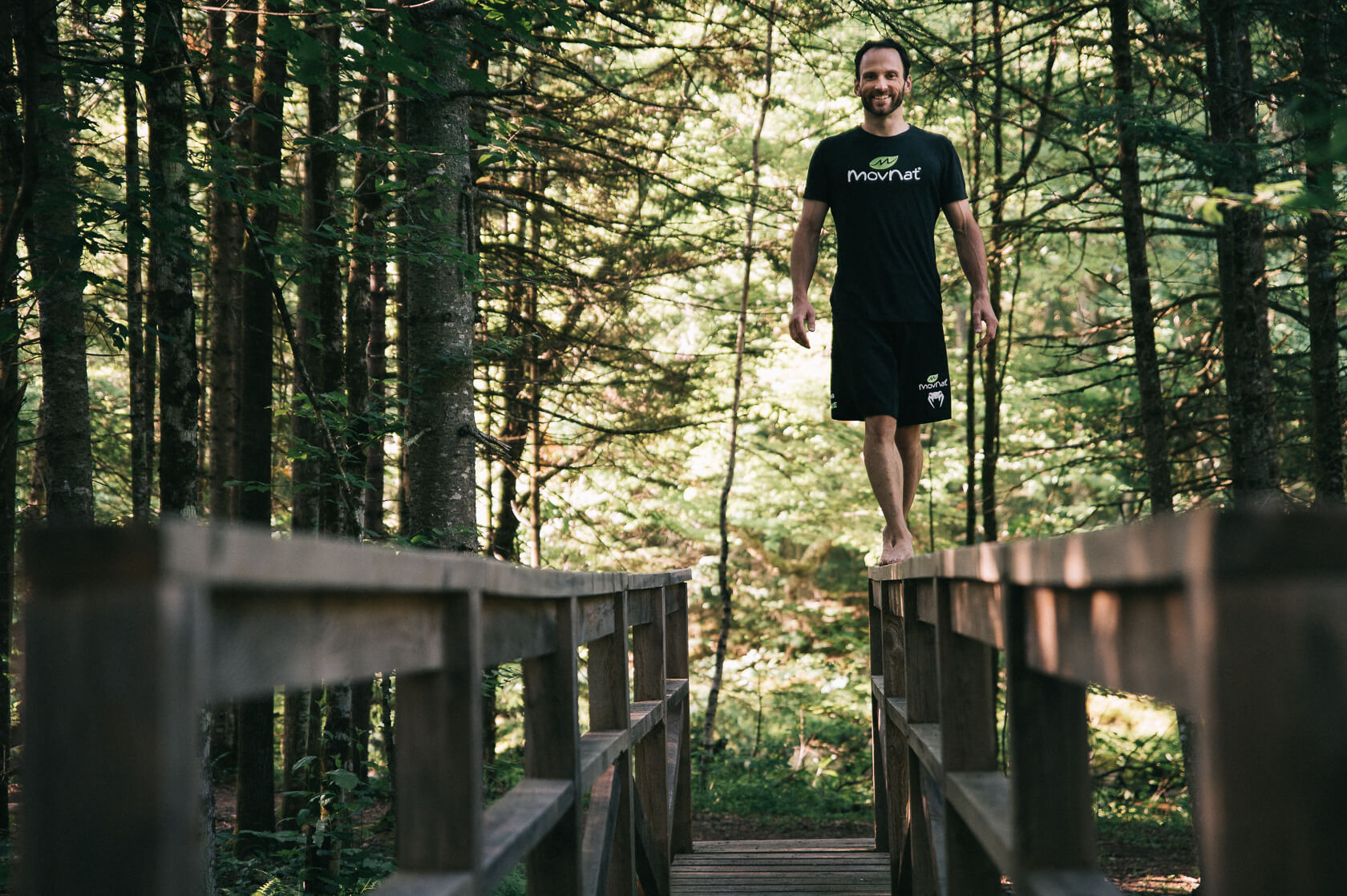 David marche en équilibre sur la main-courante d'un pont en forêt