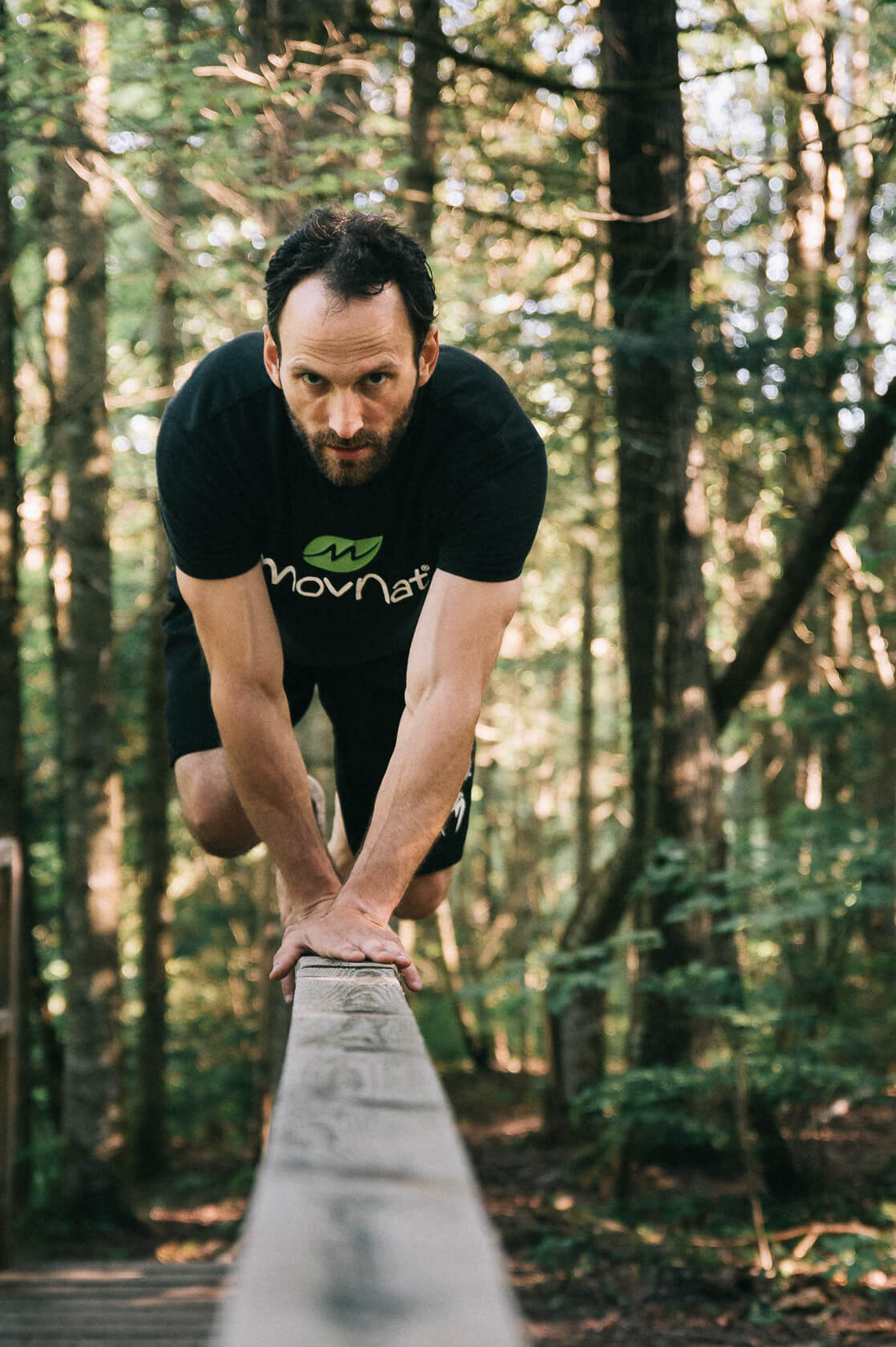 David marche à quatre pattes sur la main-courante du pont d'un sentier dans le bois